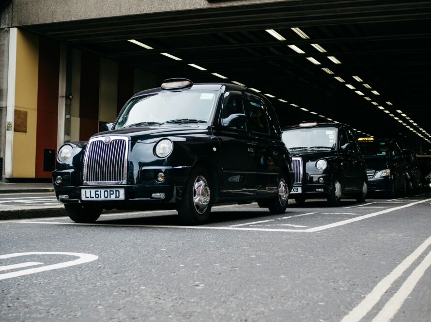 Several black taxis lined up under an urban overpass