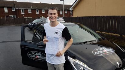 Carl standing beside a driving school car holding his test passing certificate in Belfast