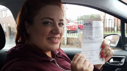 Geraldine holding her passing certificate in a car, smiling after passing her driving test in Belfast