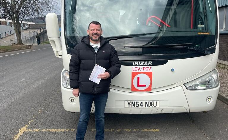 Anthony standing proudly in front of a coach after passing his PCV test.