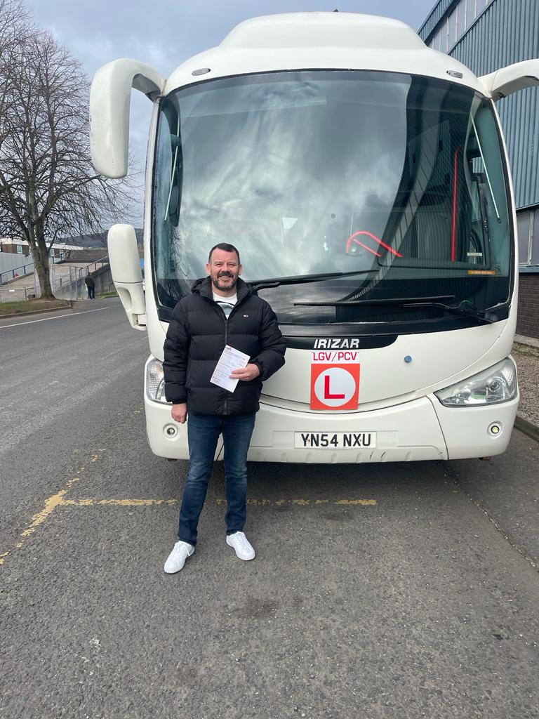 Anthony standing proudly in front of a coach after passing his PCV test.