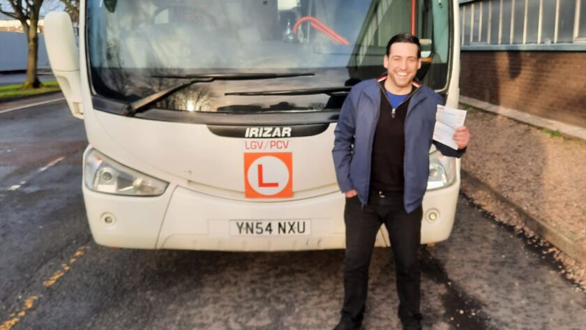 Marty smiling in front of a coach after passing his PCV test.